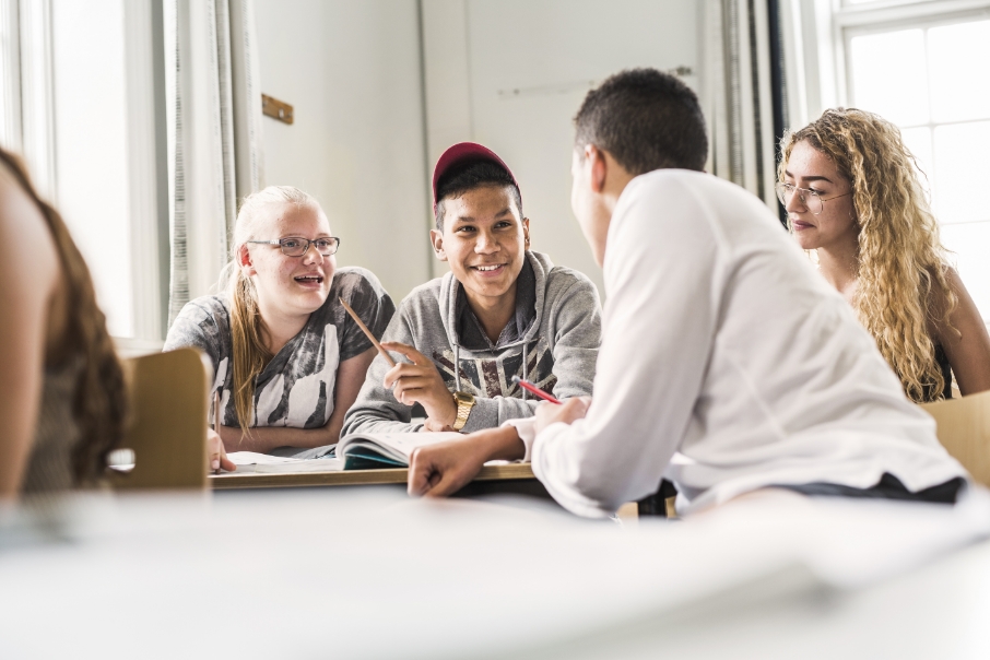 Across education setting. Four students sitting in a classroom smiling to each other.