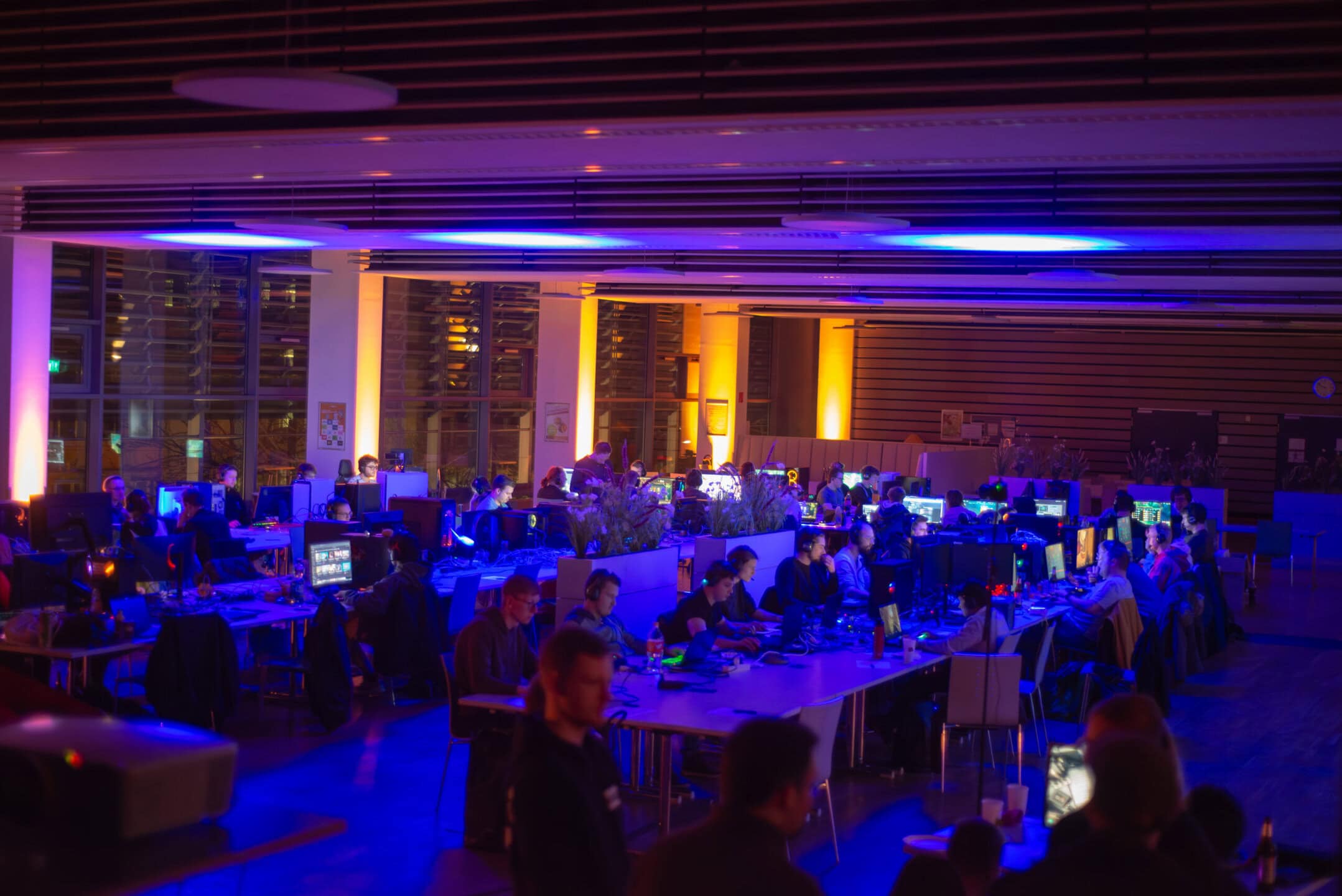 Around 60 students play computer games at a previous CampusLAN event in a darkened room at night.